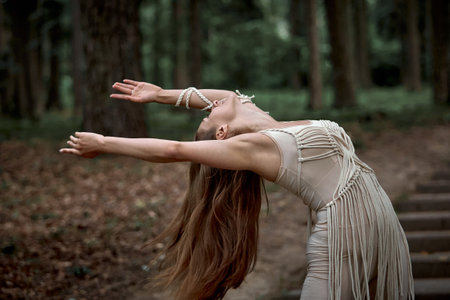 Beautiful young woman with long hair dancing in nature. Clothing made of eco-friendly materials in beige and macrame. The concept of a healthy spirit, active activity.の写真素材