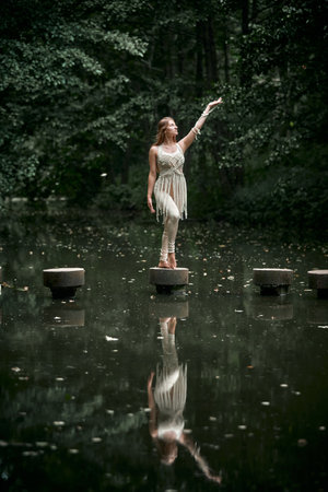 In a green forest, a young woman in a macrame dress stands on a concrete circle, her hand raised in the air. The concept of balance and natural cosmetics.の写真素材