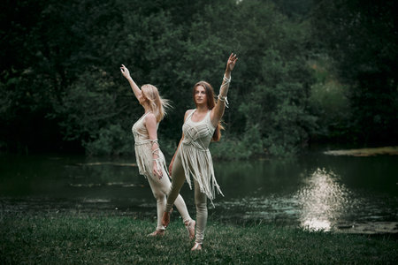 Two beautiful young women dancing in nature. There is a large lake behind. The concept of natural cosmetics and harmony with nature. My hair is blowing in the wind.の写真素材