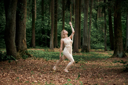 Blonde barefoot dancing in a dense forest in summer. Clothing of their eco-materials and macrame. The concept of natural products and harmony with nature.の写真素材