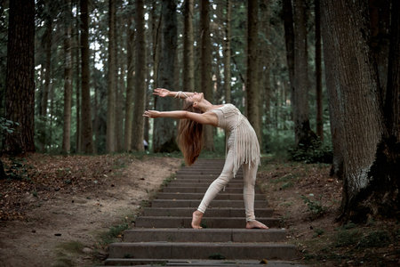 Beautiful young woman dancing in nature in summer on concrete steps. Clothing made of eco-friendly materials in beige and macrame.の写真素材