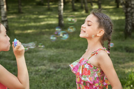 A girl lets out soap bubbles in nature, and a friend catches them. Sunny summer warm day.の写真素材
