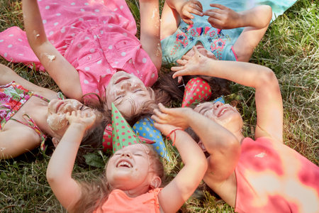 Funny girls in holiday hats are lying on the ground together. Birthday celebration in the summer in the Park.の写真素材