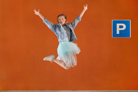 Beautiful cute blonde girl bounces up near the Parking sign. Orange background.
