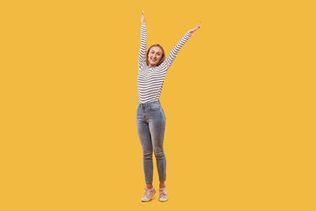 Beautiful happy blonde woman in jeans is happy and raised her hands up. Yellow background.の写真素材
