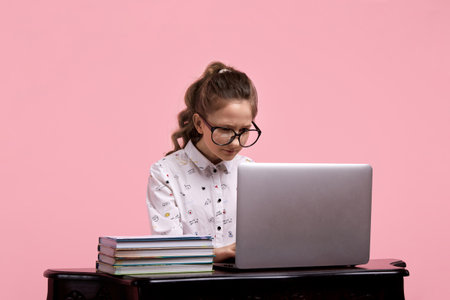 A girl with glasses and with piled hair in a ponytail sits at a wooden table and bakes something on a laptopの写真素材
