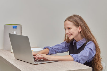 A girl with long blonde wavy hair is studying online with a laptop. School at the time of the...