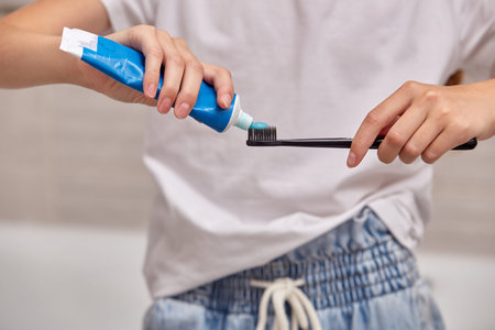 Female hands holding a black toothbrush and applying paste. Care of the oral cavity.