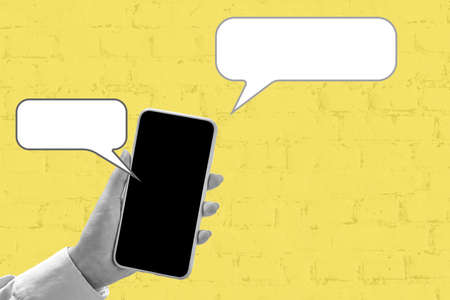 A gray female hand holding a smartphone with a blank screen. Cloud with chat. Yellow background. Trending colors.の写真素材