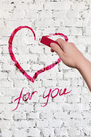 A womans hand draws a heart with pink chalk on a wall with a white brick. Valentines Day or February 14.の写真素材