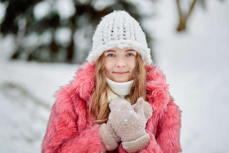 Portrait of a beautiful young woman in a winter park. Pink fur coat and white knitted hat.の写真素材