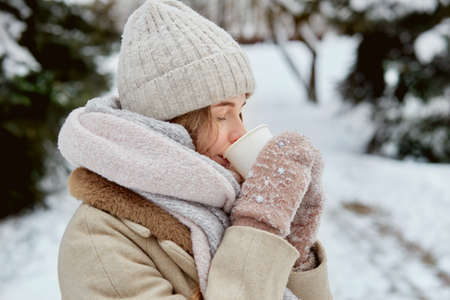 A young woman with a cup of hot tea in mittens. Beautiful winter park. Lots of white snow.の写真素材