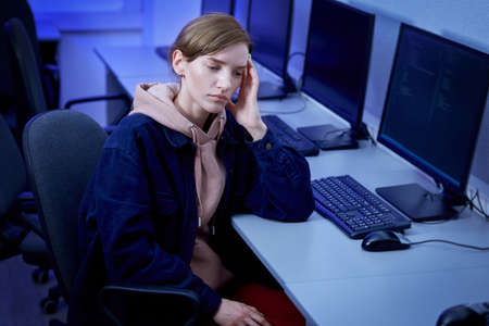 Tired young woman holding her head with her hand, headache. Office late at night. An empty office.の写真素材