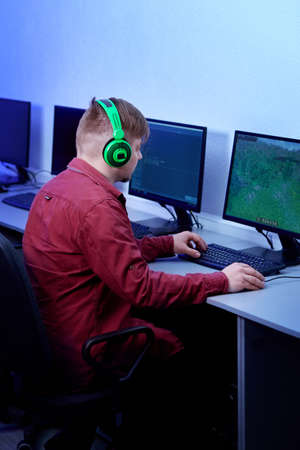 View from the back of a gamer a man plays online on his personal computer. Bright green headphones.の写真素材