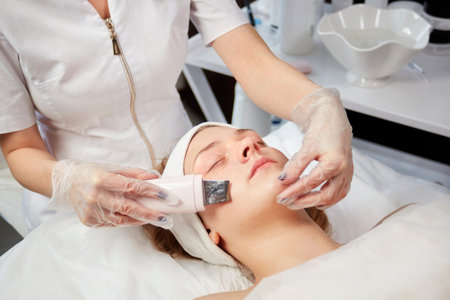 A young female cosmetologist does an electronic peeling to a client wearing gloves. Beauty salon.