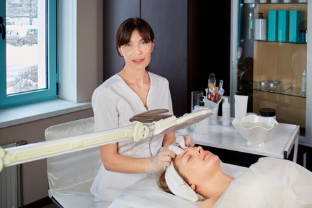 The cosmetologist cleanses the skin of the clients face and looks at the camera. Face cleansing by mechanical means. Beauty salon. Professional skin care products.の写真素材