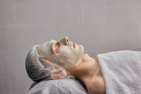 Side view of a young mans face with green natural clay in a beauty salon. Skin cleansing. Natural...