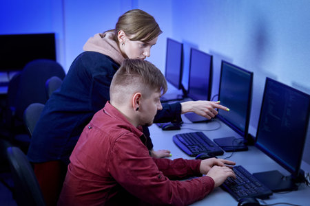 A man communicates with a colleague and discusses the work of a programmer. The woman points at the...