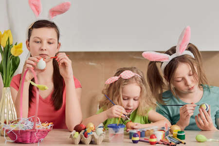 Decorate Easter eggs at home in the kitchen. Girls with a brush in their hands paint chicken eggs. Traditions. Easter holiday.の写真素材