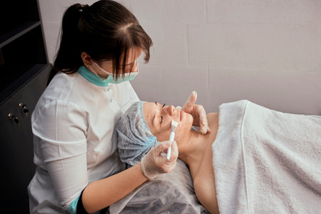 A female cosmetologist with a brush applies a cosmetic product to the clients face. Professional beauty salon.の写真素材