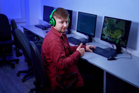 A man playing with green headphones shows a thumbs-up gesture. Happy guy plays games online.の写真素材