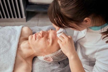 The cosmetologist removes acne with his hands and wipes on the face of a young man. Beauty salon. Professional skin care.の写真素材