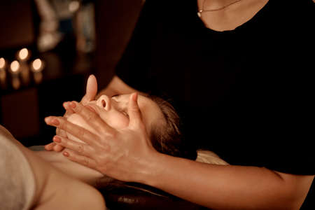 A female masseur gives a facial massage to a young woman. Wellness massage. The concept of alternative medicine.の写真素材