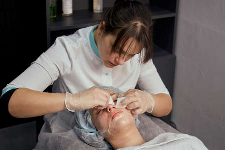 A female cosmetologist cleans her face with cotton pads for a young female patient. Professional cosmetologist.の写真素材