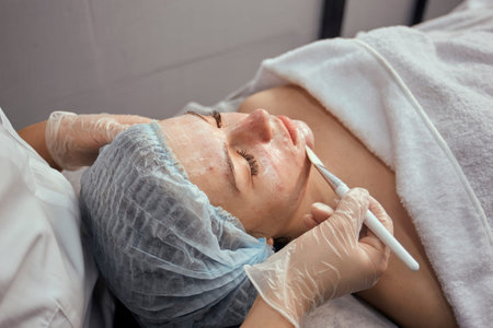 The hands of a cosmetologist in gloves are applied to the face of a female client with acne gel...