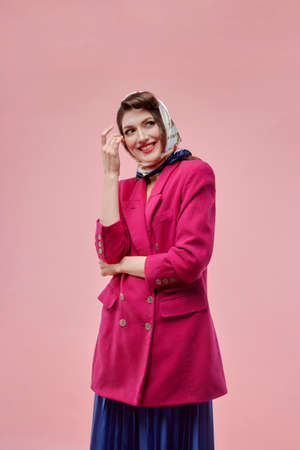A brunette woman with very bright makeup in a pink jacket and a long blue skirt. Pin-up style. Pink background.の写真素材