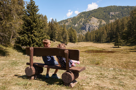 Brother and sister sit on a wooden bench in the mountains. Stop while walking. Summer holidays.の写真素材
