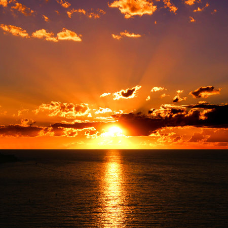 Vibrant sunset over the ocean with clouds and sunbeamsの写真素材