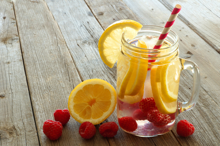 Vitamin water with lemon and raspberries in a jar with straw against a wood backgroundの写真素材