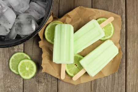 Homemade lime yogurt popsicles with fresh lime slices on paper with rustic wood backgroundの写真素材