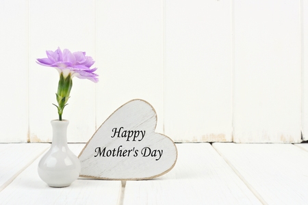 Happy Mothers Day tag with small vase and single purple carnation flower against a white backgroundの写真素材