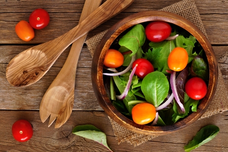 Mixed salad with cherry tomatoes and red onions in wooden bowl overhead scene on rustic woodの写真素材