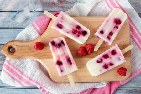 Homemade raspberry vanilla ice pops on a paddle board with towel on a rustic wood backgroundの写真素材