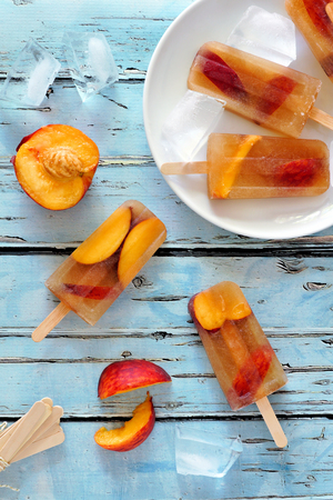 Homemade peach iced tea popsicles, overhead scene on rustic blue woodの写真素材