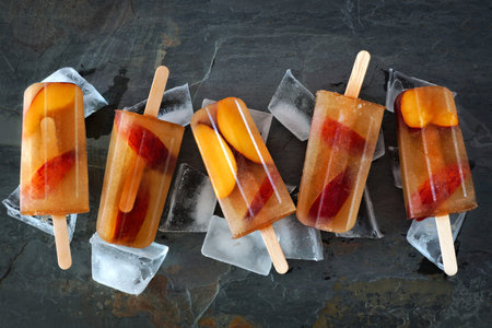 Group of peach iced tea popsicles with ice on a slate stone background
