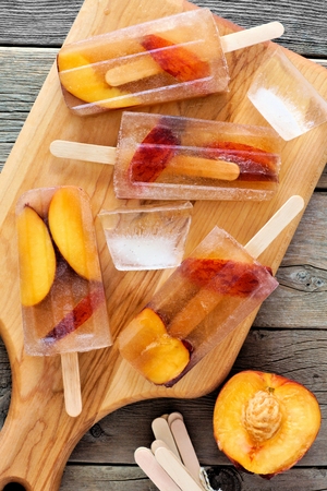 Homemade peach iced tea popsicles, on paddle board against rustic wooden backgroundの写真素材
