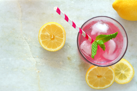 Glass of pink lemonade with mint and lemon slices overhead view on a white marble backgroundの写真素材