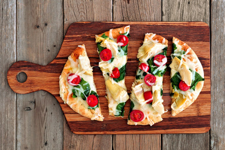 Healthy flat bread pizza with melted mozzarella, tomatoes, spinach and artichokes, above view on wooden paddle boardの写真素材