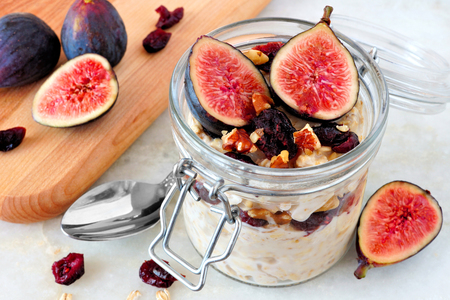 Jar of overnight autumn oats with red figs, cranberries and walnuts against a marble backgroundの写真素材