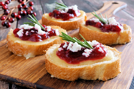 Holiday crostini appetizers with cranberry sauce, brie, feta and rosemary on a wooden serverの写真素材