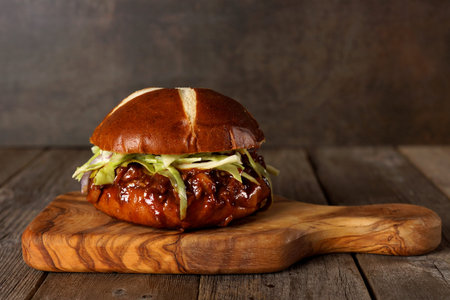 Pulled pork burger on pretzel bun on a serving board with wood backgroundの写真素材