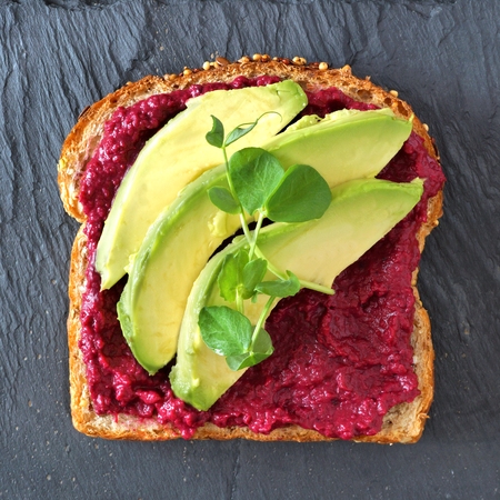 Beet hummus and avocado toast with pea shoots, overhead view on a slate backgroundの写真素材