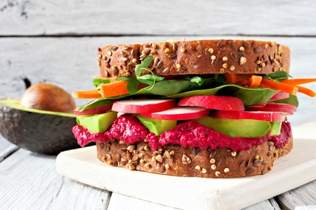 Superfood sandwich with beet hummus, avocado, vegetables and greens, on whole grain bread against a white wood backgroundの写真素材