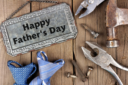 Happy Fathers Day greeting on metal sign with tools and ties on a wooden background
