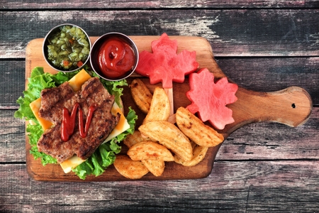 Canada Day picnic scene with maple leaf shaped hamburger and watermelon on a paddle board over rustic woodの写真素材