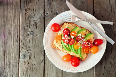 Avocado toast with hummus and tomatoes on plate, above view on old wood backgroundの写真素材